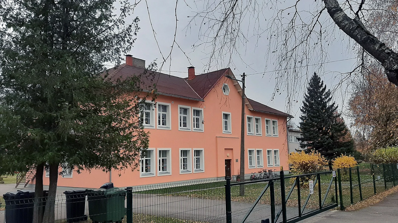 Zweistöckiges Kindergartengebäude hinter einem Zaun, davor Bäume im Herbstlaub